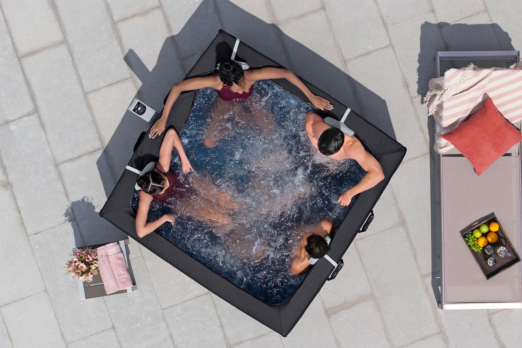 People relaxing in a hot tub on a patio with a table and fruit bowl nearby.