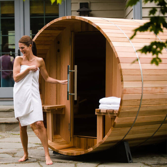 Woman standing next to a Audra wooden outdoor sauna with towels inside