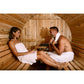 Two people sitting in a Almost Heaven Pinnacle wooden sauna, wrapped in towels.