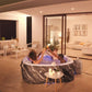 People in a hot tub on a patio at night with a modern house interior visible.