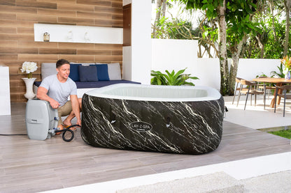 Man sitting next to a portable hot tub on a wooden deck with a modern interior background.
