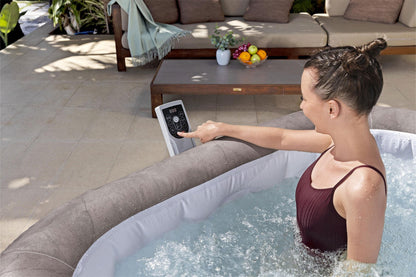 Woman in a hot tub using a remote control with an outdoor setting in the background.