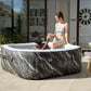 Two women in a marble-patterned inflatable hot tub in a modern living room.