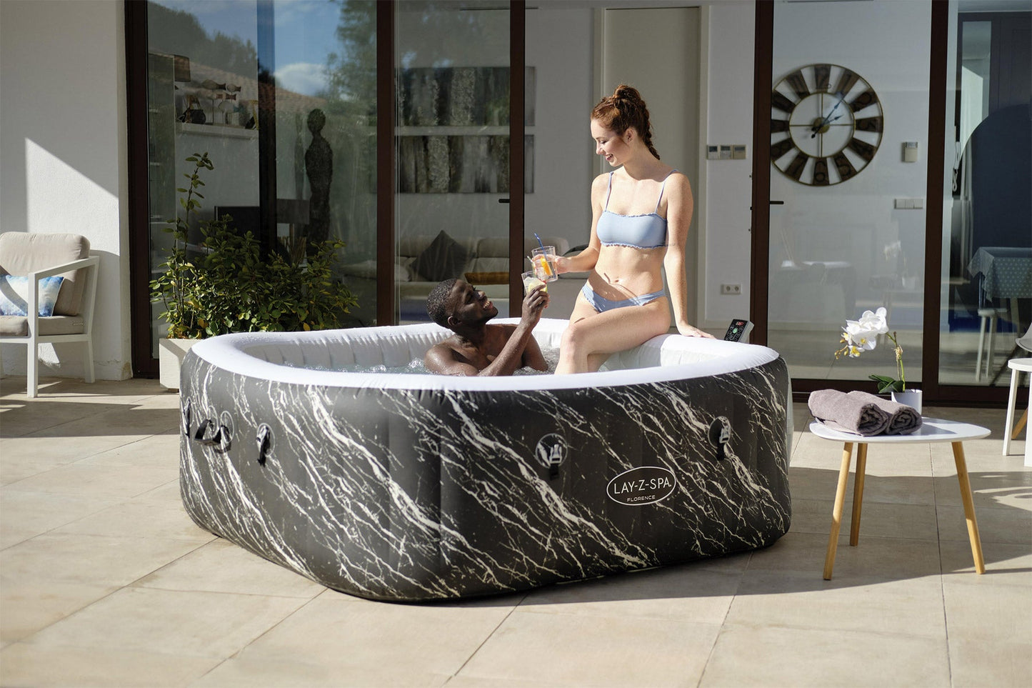Two women in a marble-patterned inflatable hot tub in a modern living room.