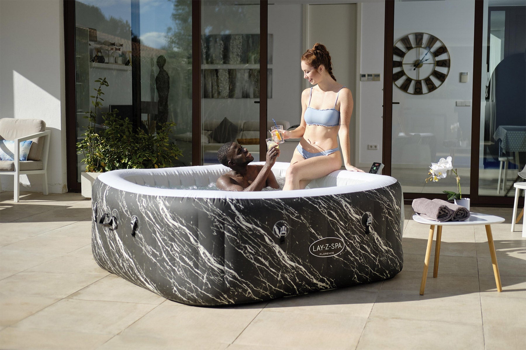 Two women in a marble-patterned inflatable hot tub in a modern living room.