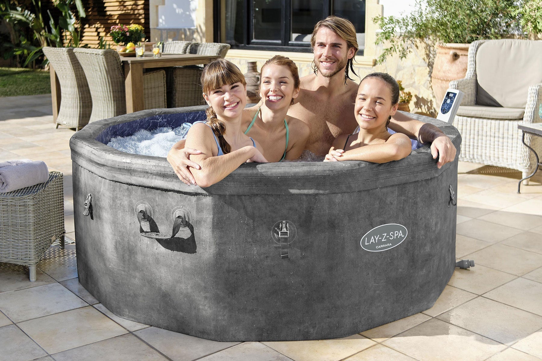 Family of four in a Lay-Z-Spa hot tub outdoors on a sunny day.