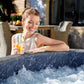 Woman relaxing in a hot tub with a drink, surrounded by outdoor furniture.