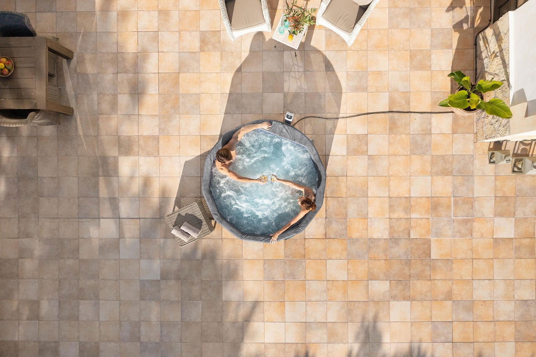 Top-down view of a person relaxing in a hot tub on a tiled patio.