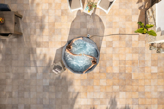 Top-down view of a person relaxing in a hot tub on a tiled patio.
