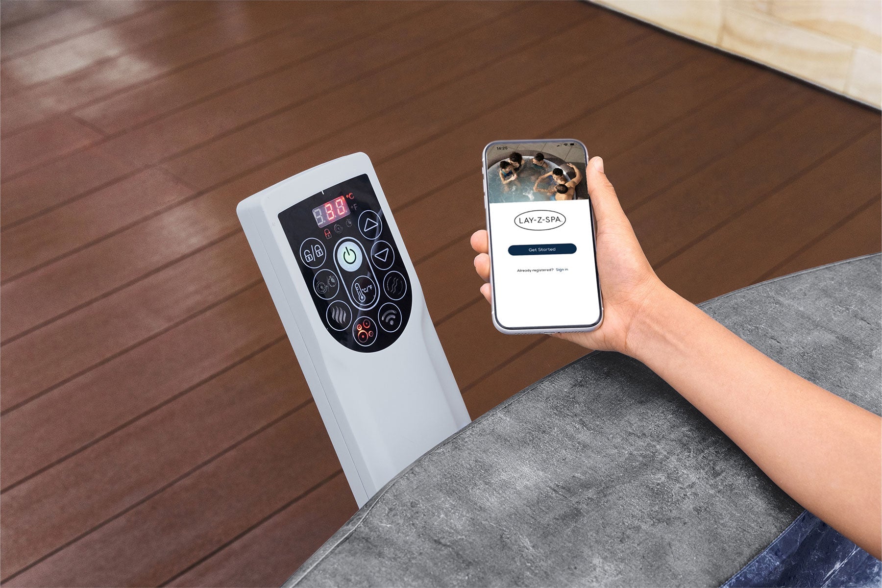 Person using a smartphone app to control an air conditioner with a remote on a wooden floor.