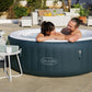 Two people in a Lay-Z-Spa inflatable hot tub on a patio with outdoor furniture.
