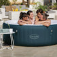 Inflatable hot tub with 'Lay-Z-Spa' branding, people around it, and outdoor setting.