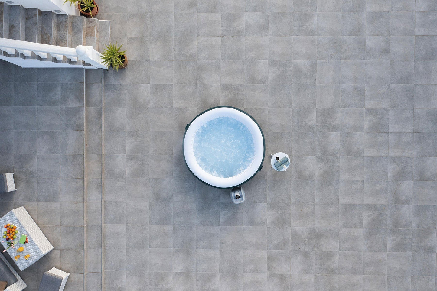 Top-down view of a hot tub on a stone patio with plants and furniture around.