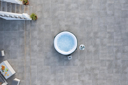 Top-down view of a hot tub on a stone patio with plants and furniture around.