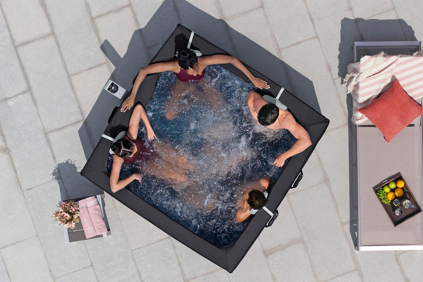 People relaxing in a hot tub on a patio with a table and fruit bowl nearby.