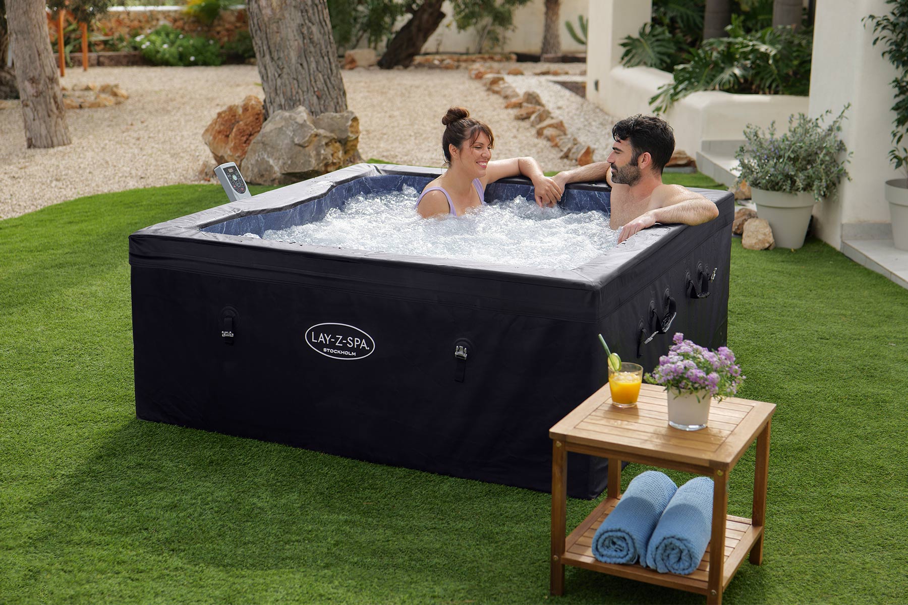 Two people in a hot tub with a table next to it on a grassy area.