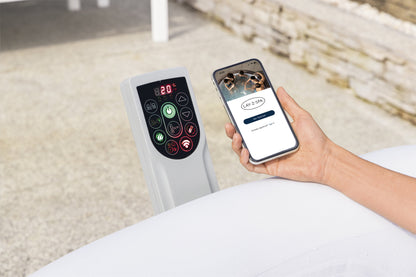 Hand holding a smartphone with a control app next to a remote control on a bed.