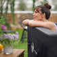 Woman relaxing by a hot tub with flowers and a drink on a table in the foreground.