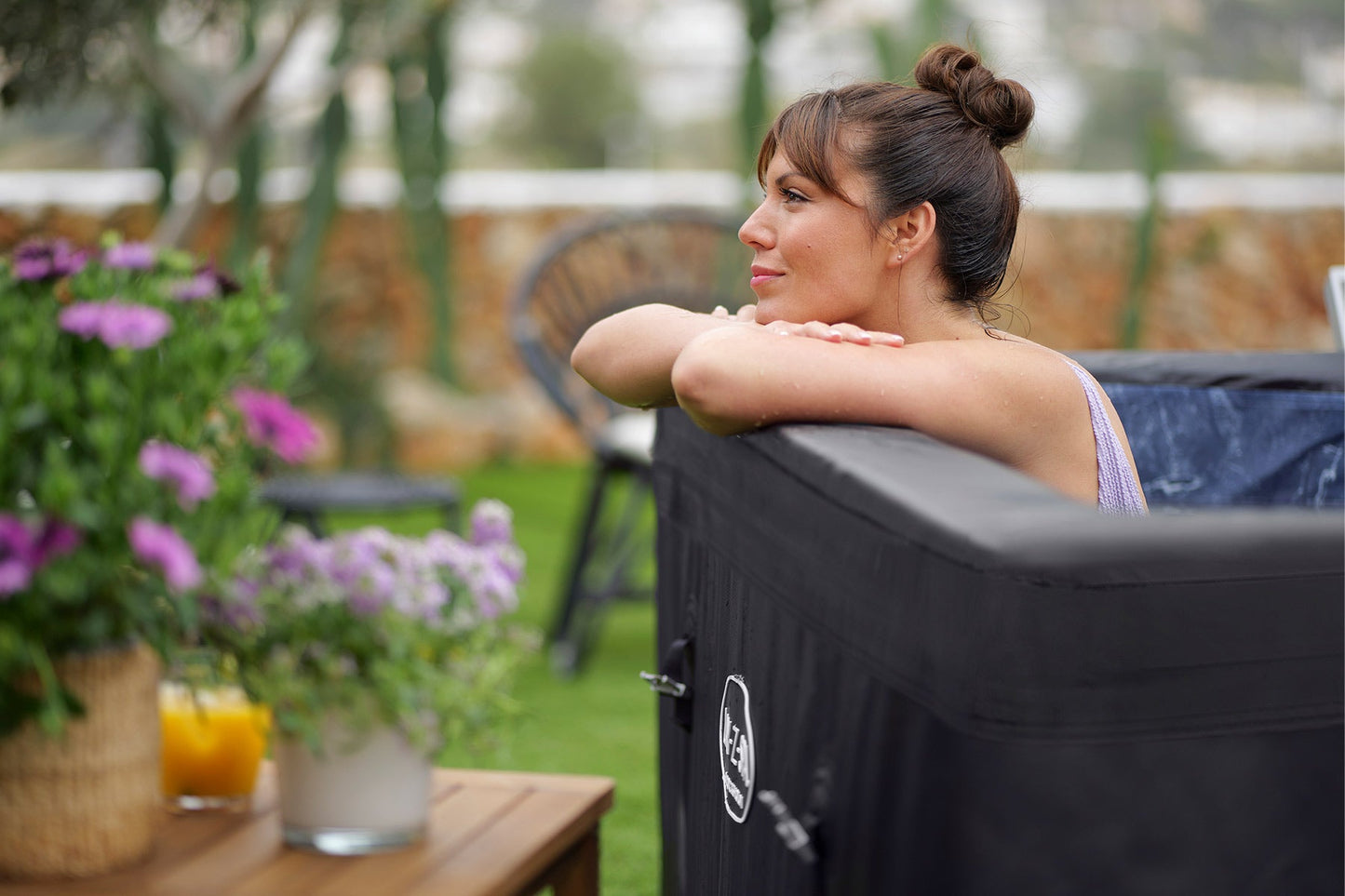 Woman relaxing by a hot tub with flowers and a drink on a table in the foreground.